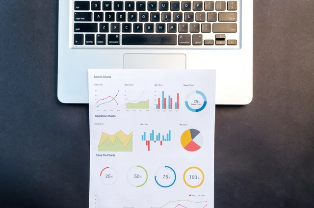 Top-down view of a laptop keyboard and colorful printed charts on a desk. Comparing five conversion delivery models against an in-house baseline
